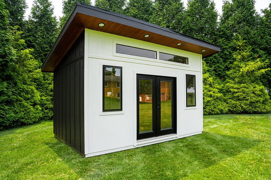 A small black and white shed in the middle of a green yard.